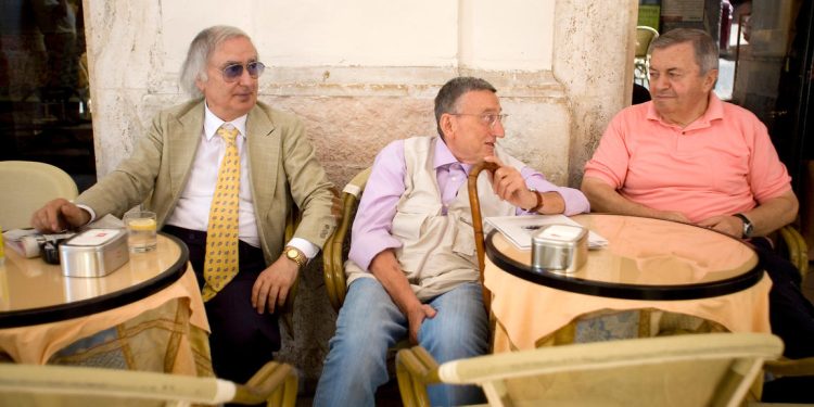 Three old men sit and talk at an outdoor cafe in Urbino, Italy