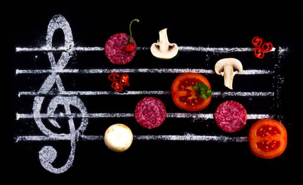 Concept of cooking pizza, like notes from ingredients. Salami, tomato and mozzarella cheese on a black background with a treble clef.